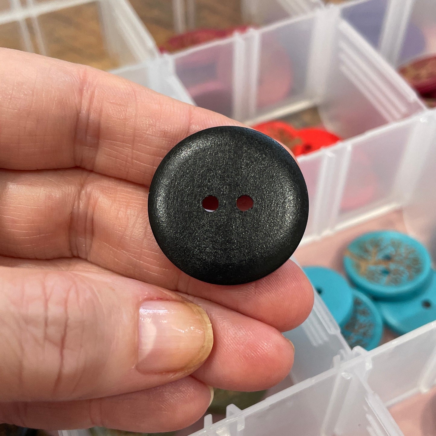 Black button held by a hand with a container of buttons in the background