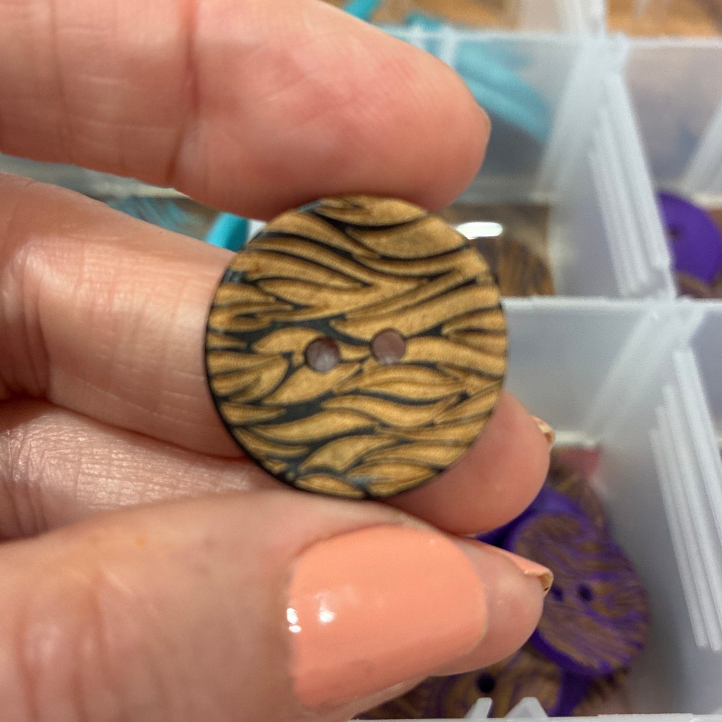 Hand holding a button with a tiger stripe pattern in front of a container of buttons.