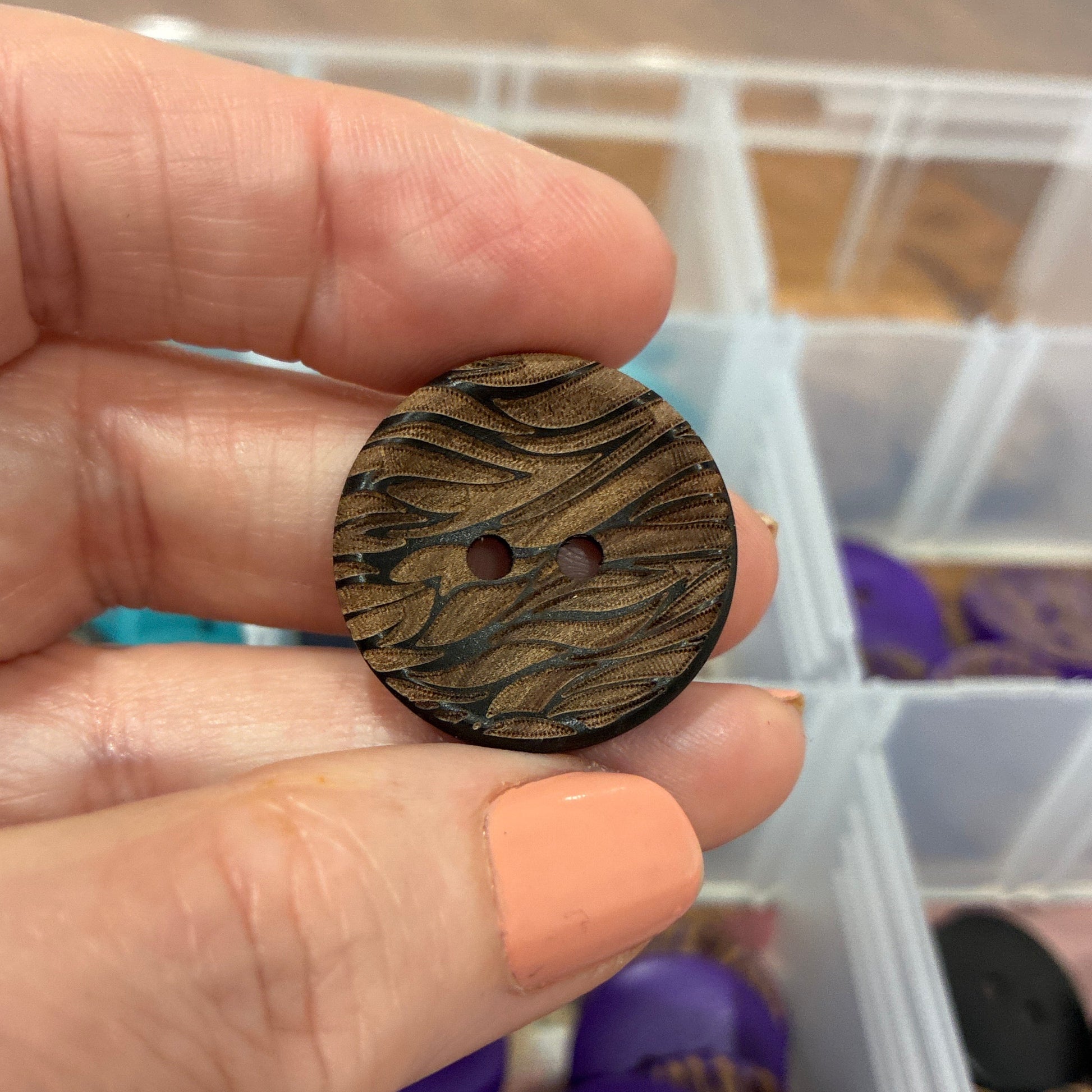 Hand holding a wooden button with a container of buttons in the background