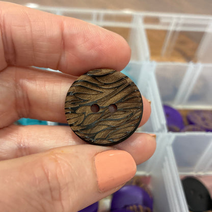 Hand holding a wooden button with a container of buttons in the background