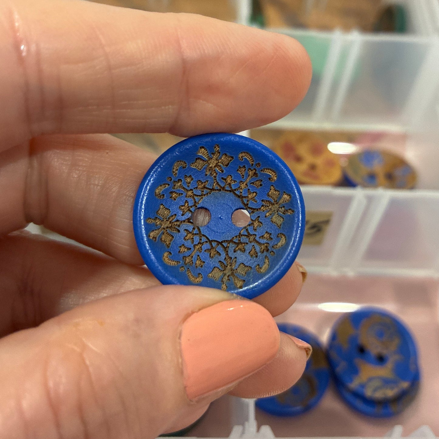 Hand holding a blue decorative button with a clear container of buttons in the background