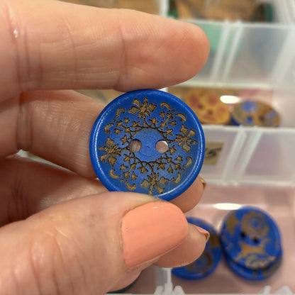 Hand holding a blue decorative button with a clear container of buttons in the background