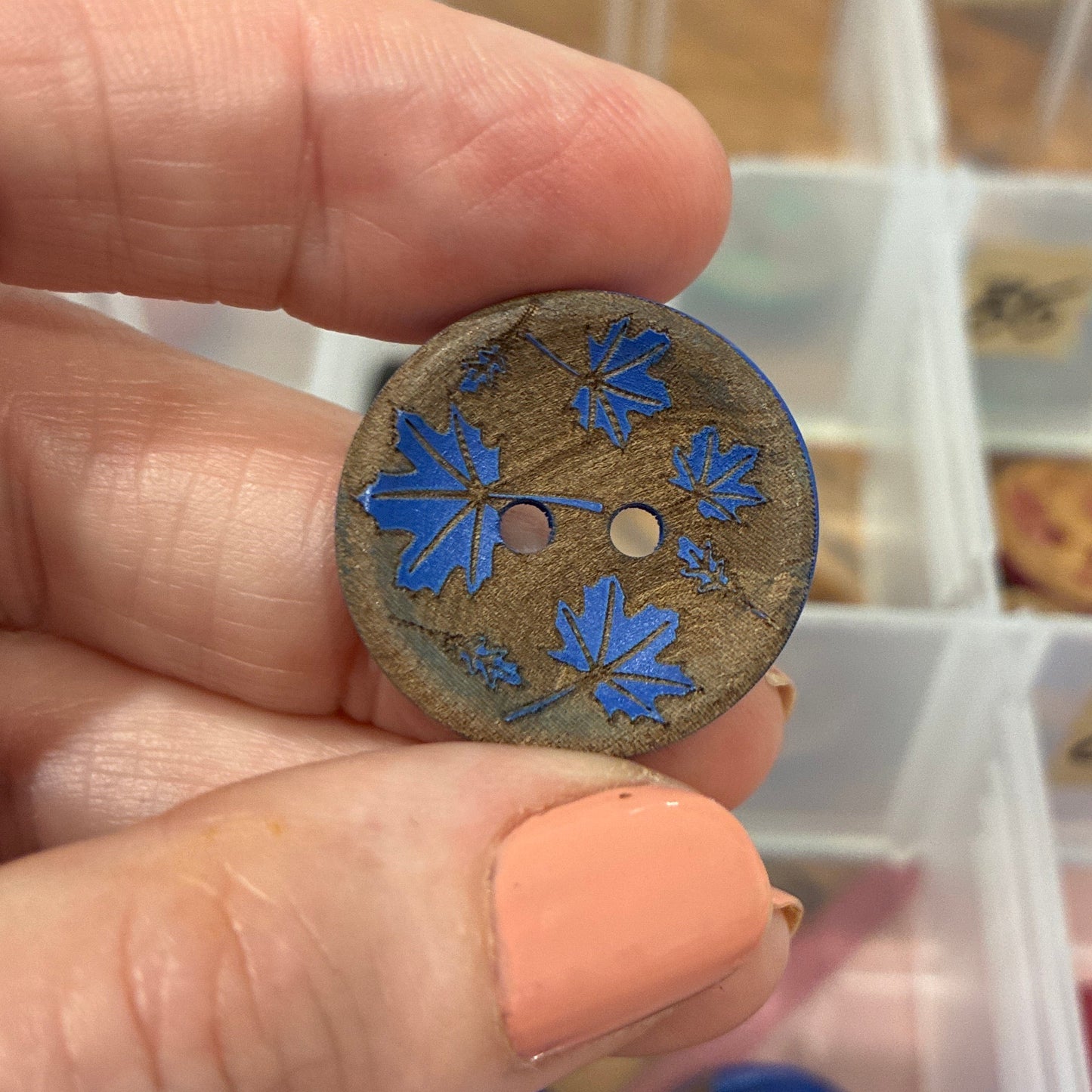 Hand holding a decorative button with blue floral design against a background of button collection.