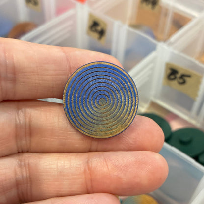 Hand holding a metallic spiral button with a colorful assortment of buttons in the background.