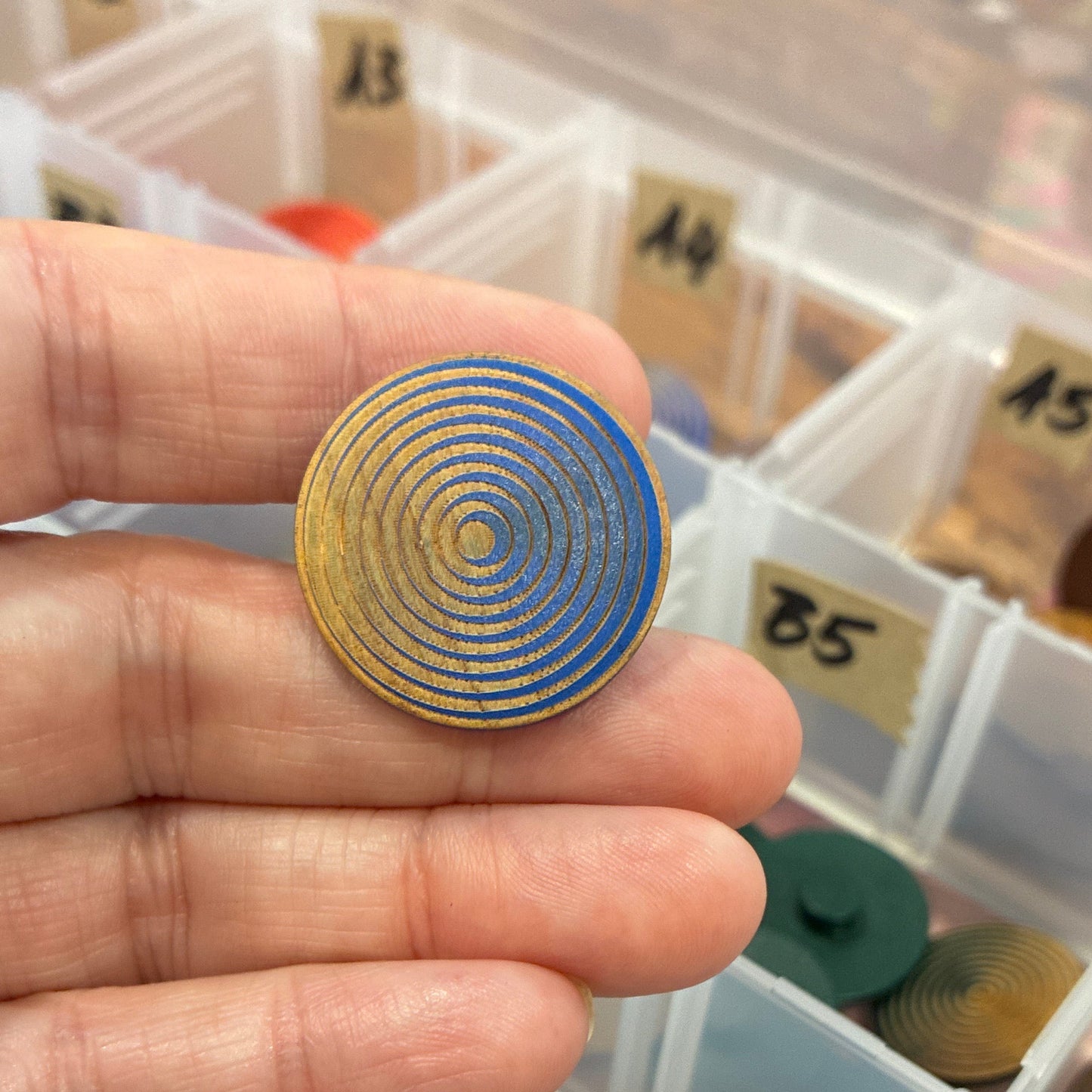 Hand holding a gold spiral button with a display case of various button in the background