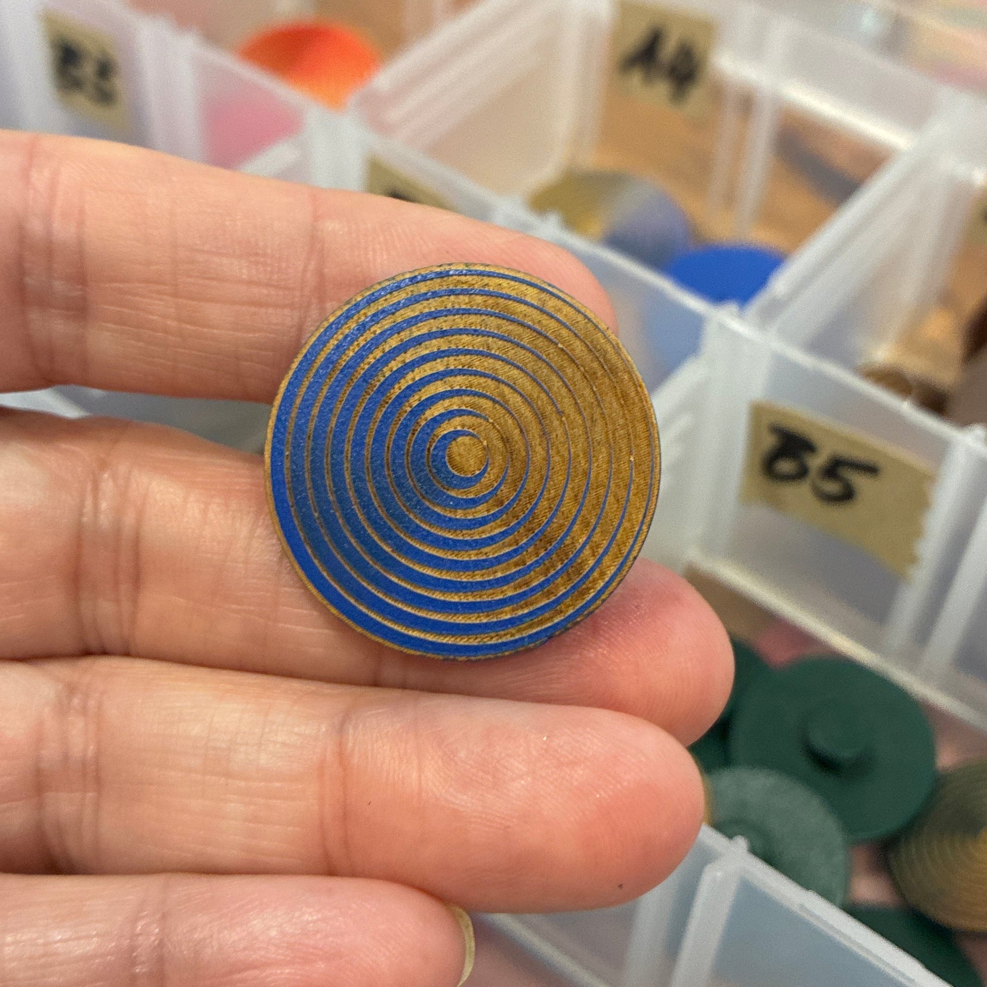 Hand holding a blue spiral button with a container of similar objects in the background