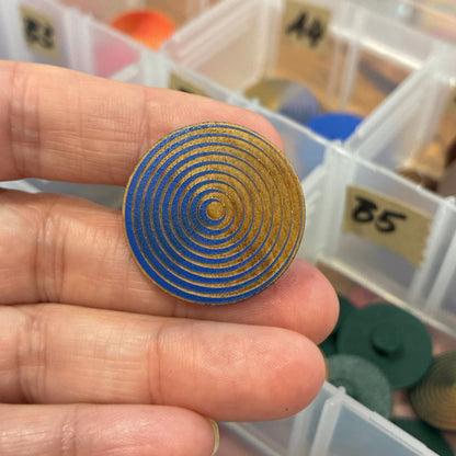 Hand holding a blue spiral button with a container of similar objects in the background
