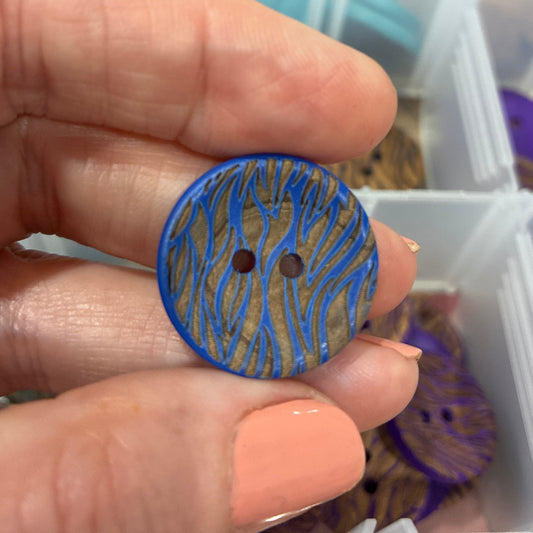 Hand holding a blue patterned button with a blurred background of a storage container.