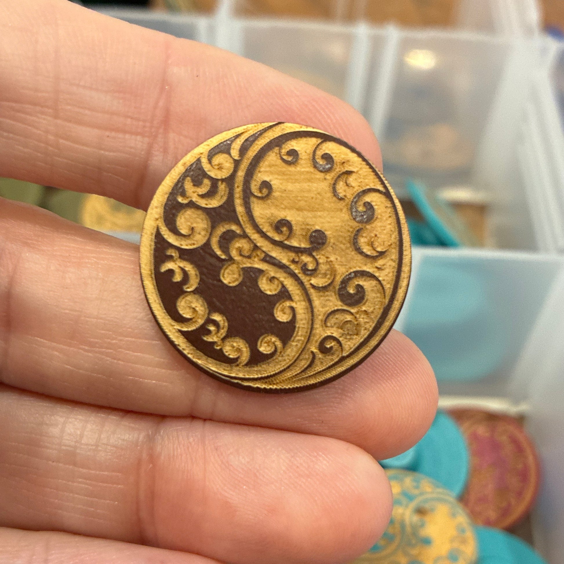 Gold decorative button held between fingers with a colorful container of buttons in the background