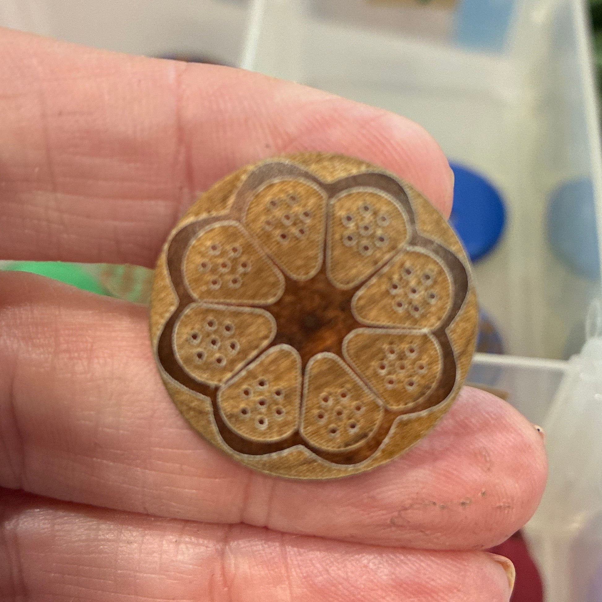Hand holding a decorative button with a floral pattern in front of a container of assorted buttons.