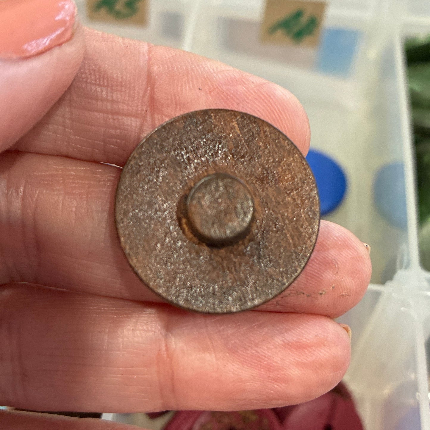 Hand holding a round button with a container of colorful buttons in the background
