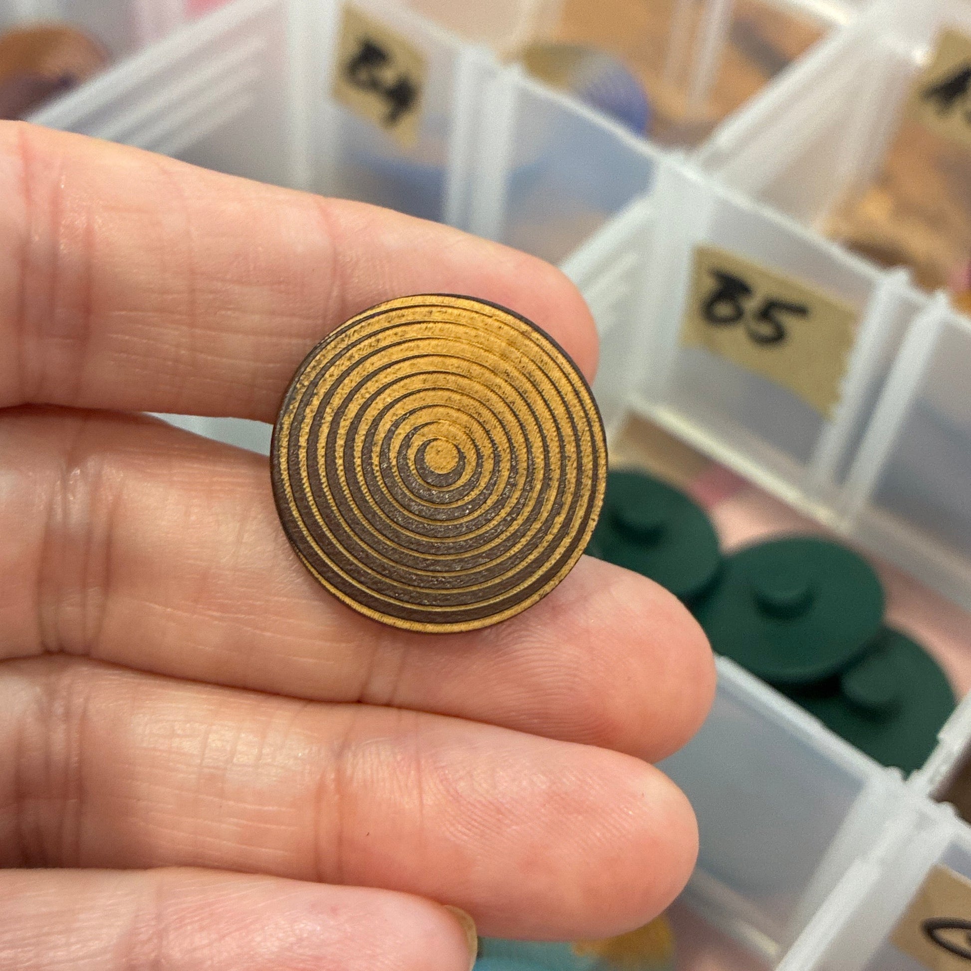 Gold spiral button held in a hand with a colorful assortment of buttons in the background.