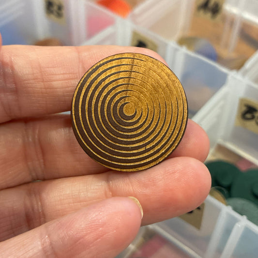 Gold spiral design held by a hand with a background of color swatches.