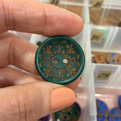 Hand holding a decorative button with a background of a container with more buttons.