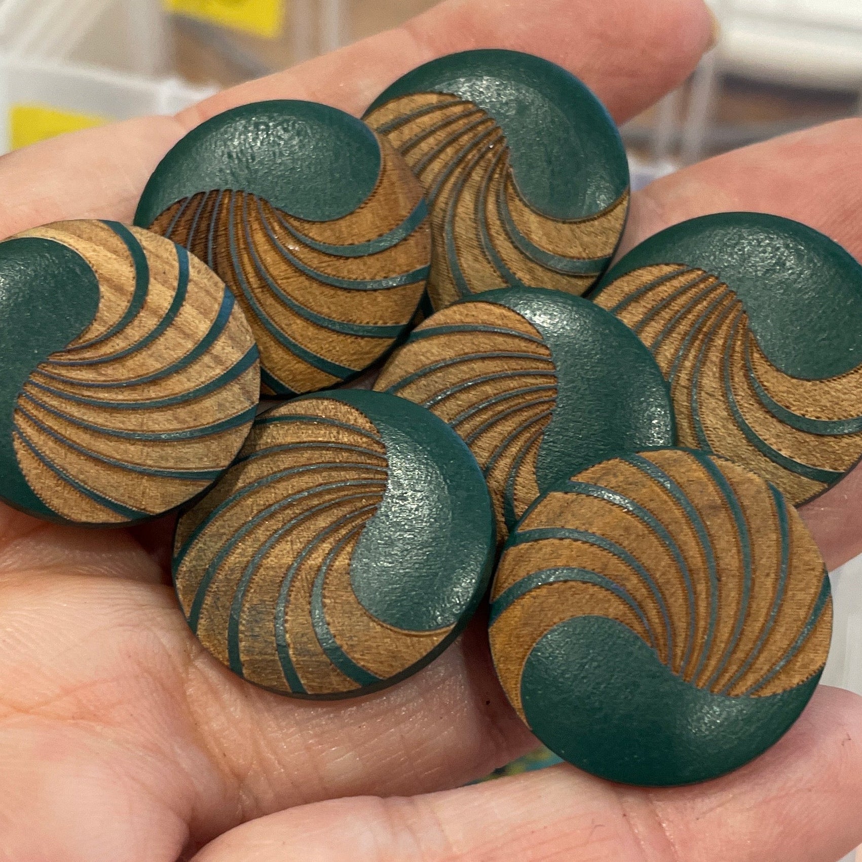 Hand holding green buttons with brown patterns against a background of button containers.