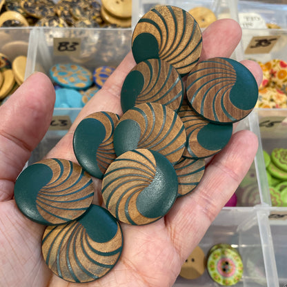 Hand holding green and gold patterned buttons with a background of button collection.
