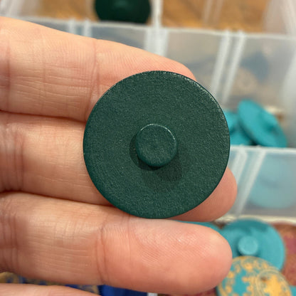 Green button held by a hand with a container of colorful buttons in the background