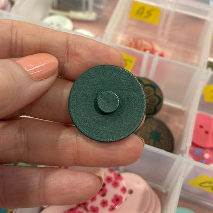 Hand holding a green button with a container of colorful buttons in the background