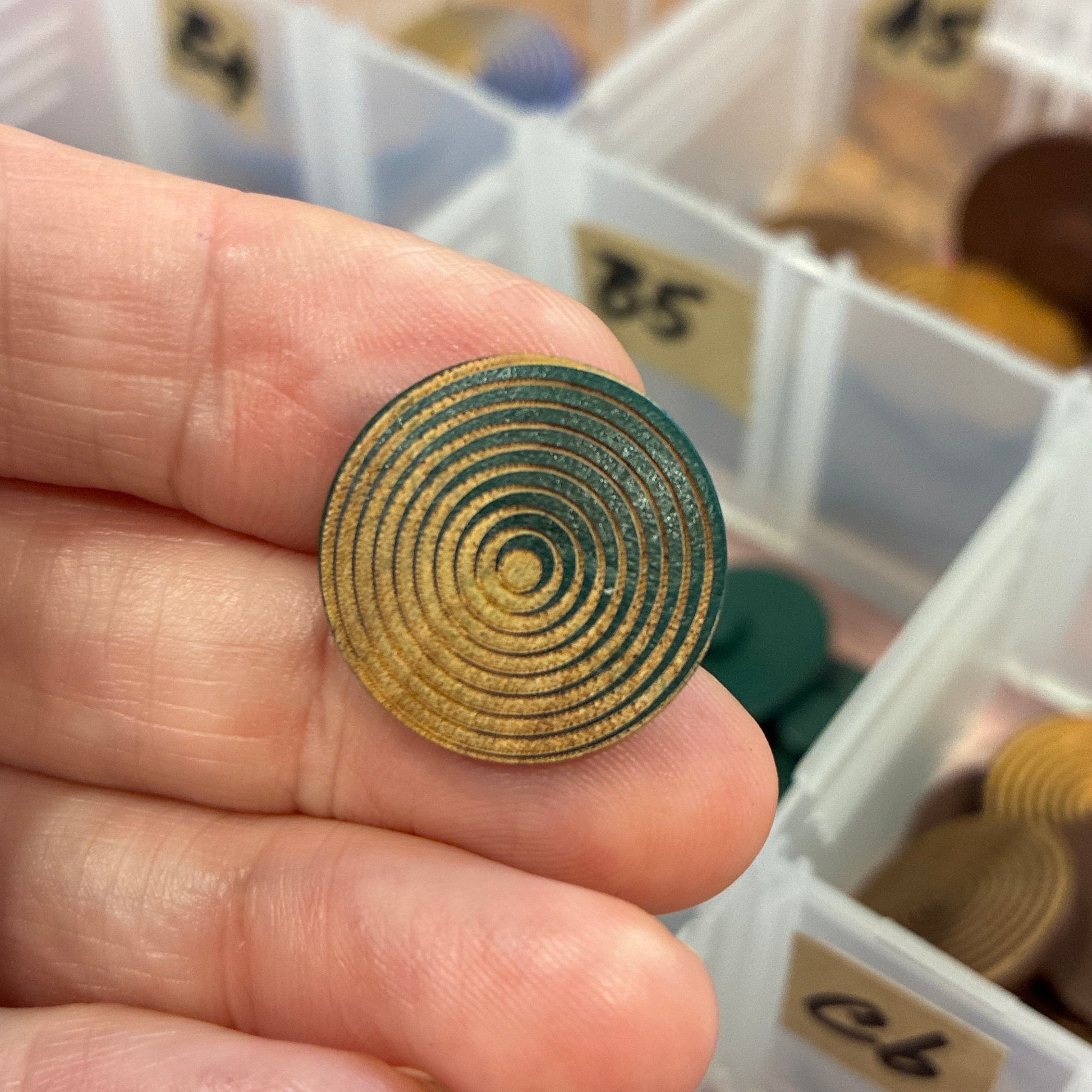 Hand holding a gold button with a container of buttons in the background