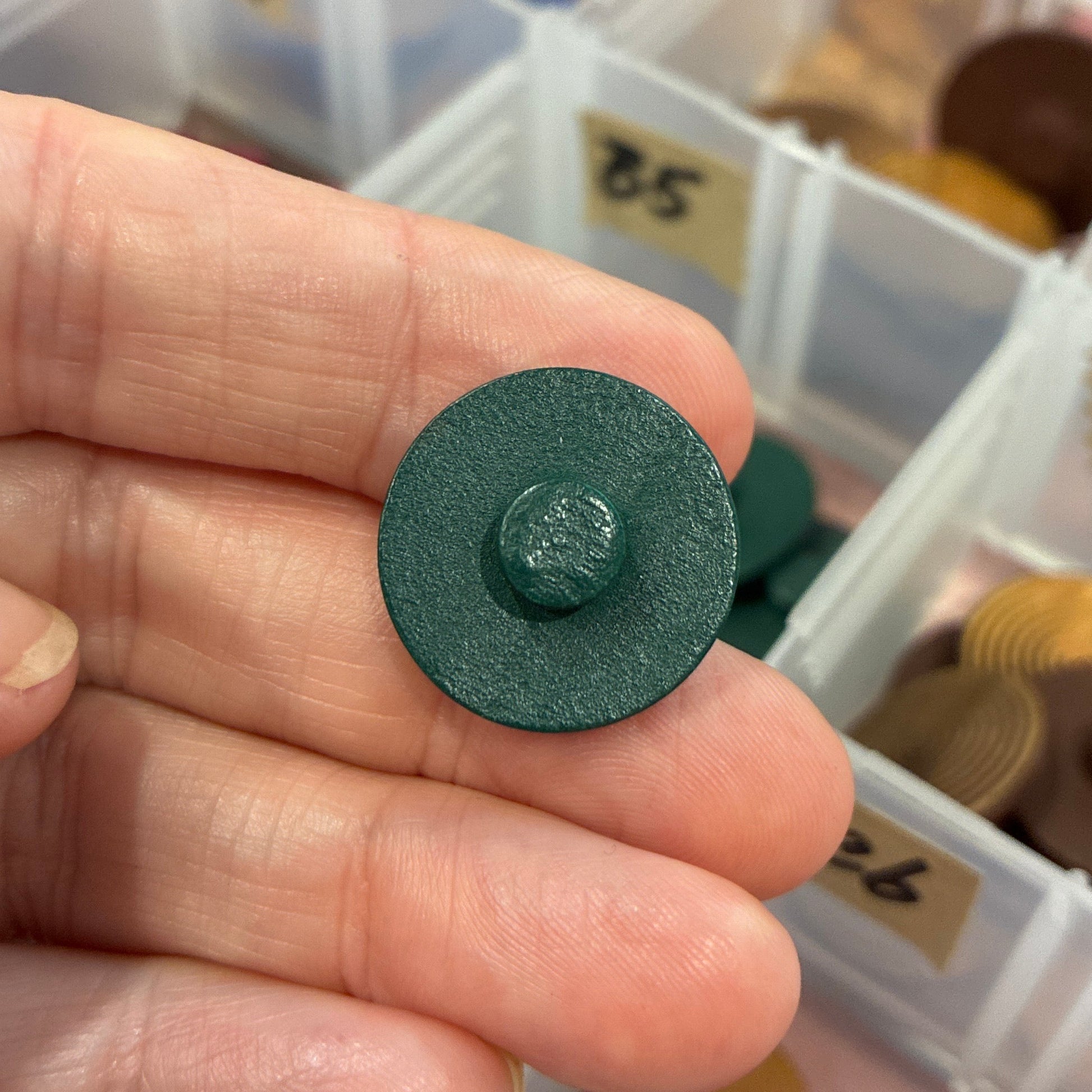 Green button held by a hand with a container of buttons in the background