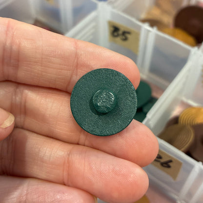 Green button held by a hand with a container of buttons in the background