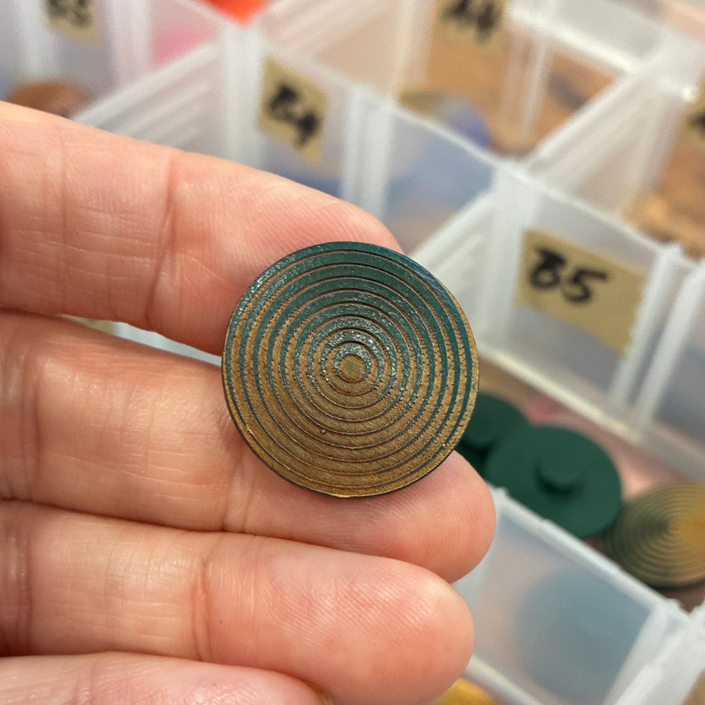 Hand holding a decorative button with a background of color swatches in a box.