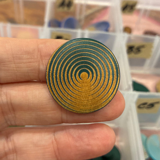 Gold spiral design on a button with a blurred background of colorful items