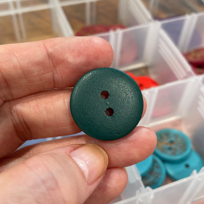 Hand holding a green button with a clear container of buttons in the background