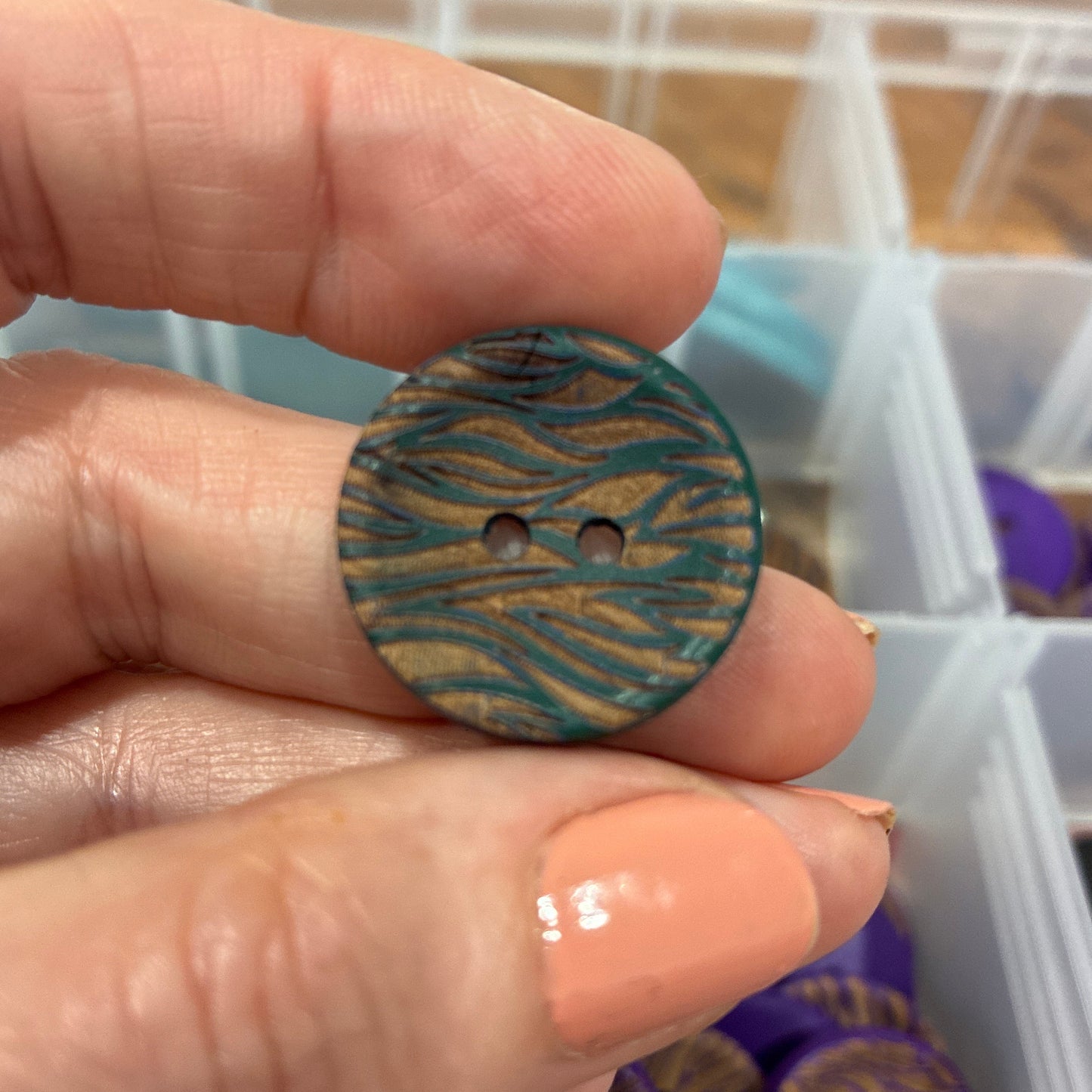 Hand holding a wooden button with a zebra pattern against a background of more buttons in a container.