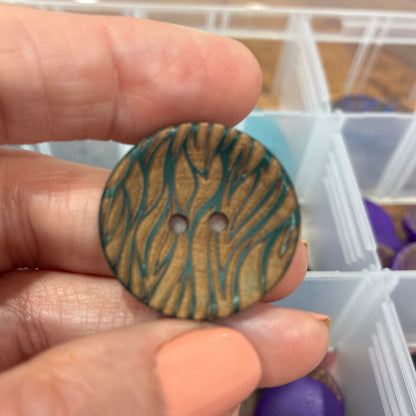 Hand holding a wooden button with a zebra pattern, with a container of buttons in the background.