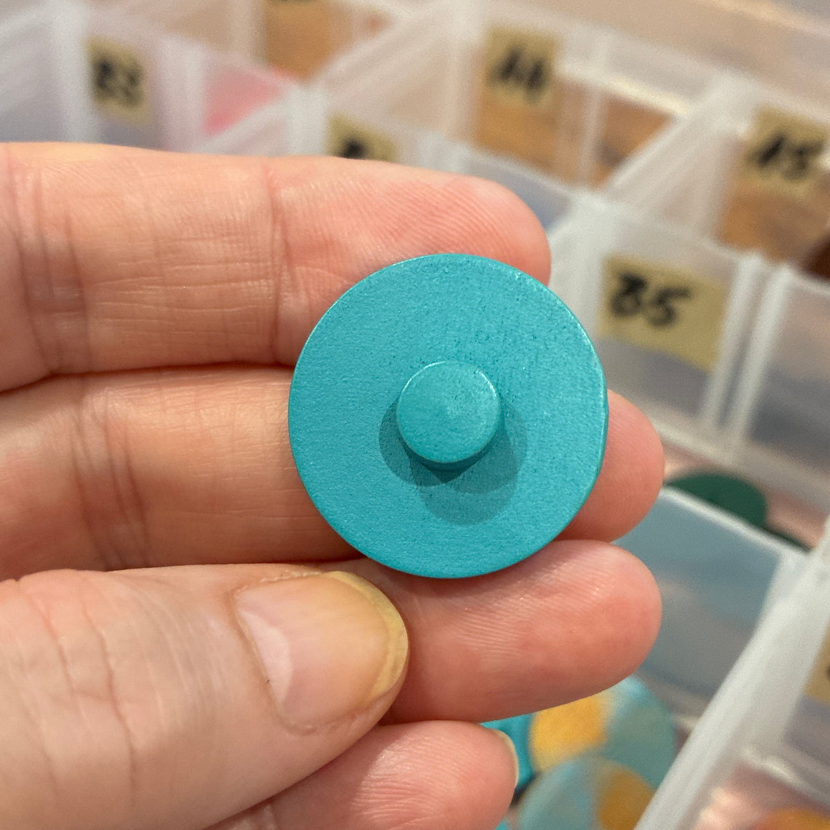 Hand holding a blue circular button with a blurred background of a storage box with compartments.