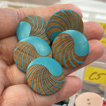 Hand holding blue and gold decorative buttons with a button collection container in the background.