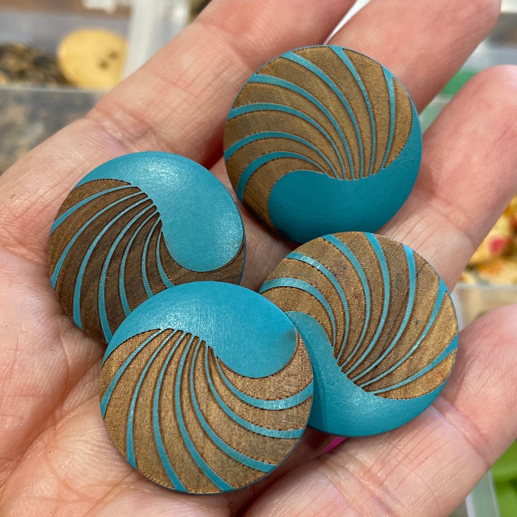 Hand holding three blue buttons with gold patterns against a blurred background of button collection.
