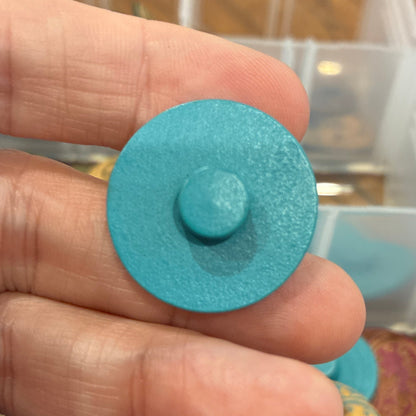 Close-up of a hand holding a blue circular object with a container of colorful objects in the background.