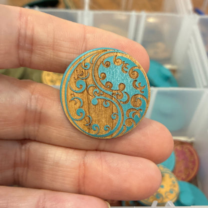 Hand holding a decorative button with intricate design, against a background of organized buttons in containers.