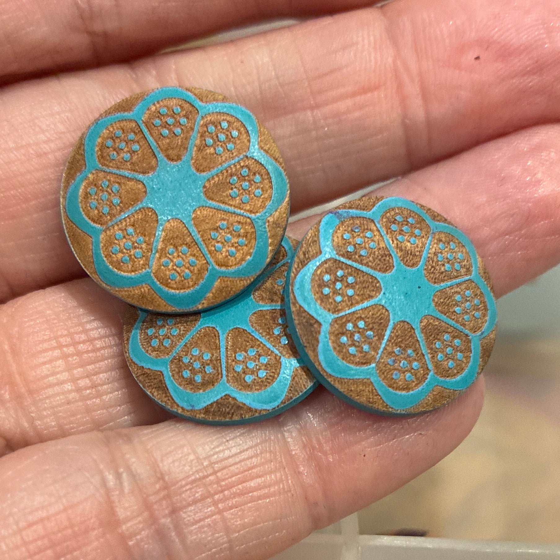 Hand holding blue and gold decorative buttons with a box of assorted buttons in the background.
