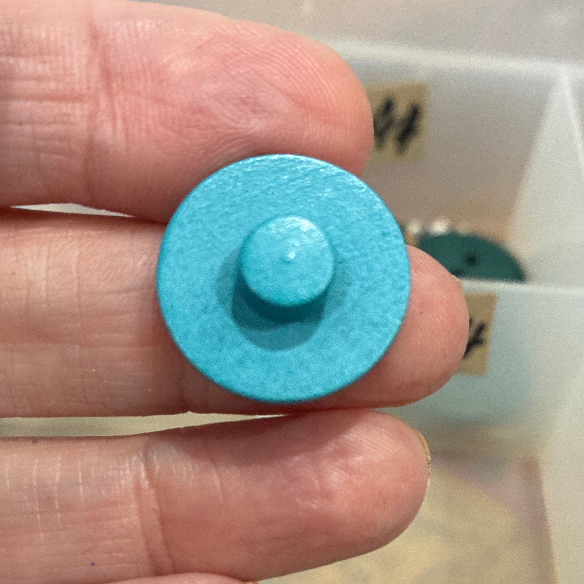 Hand holding a blue round object with a collection of colorful round objects in the background.