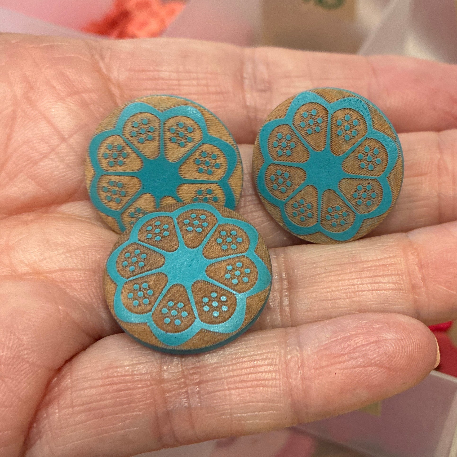 Hand holding two blue floral buttons with a container of colorful buttons in the background.