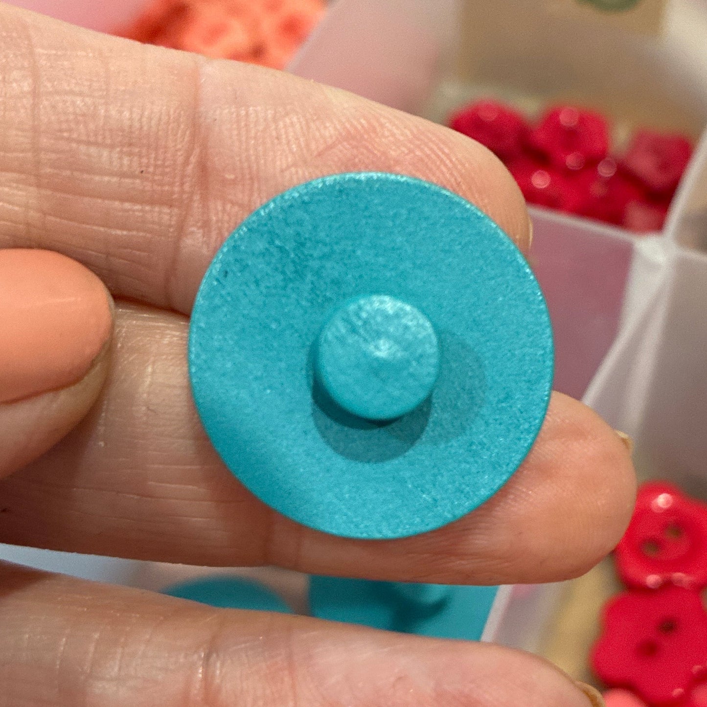 Hand holding a blue button with a container of buttons in the background