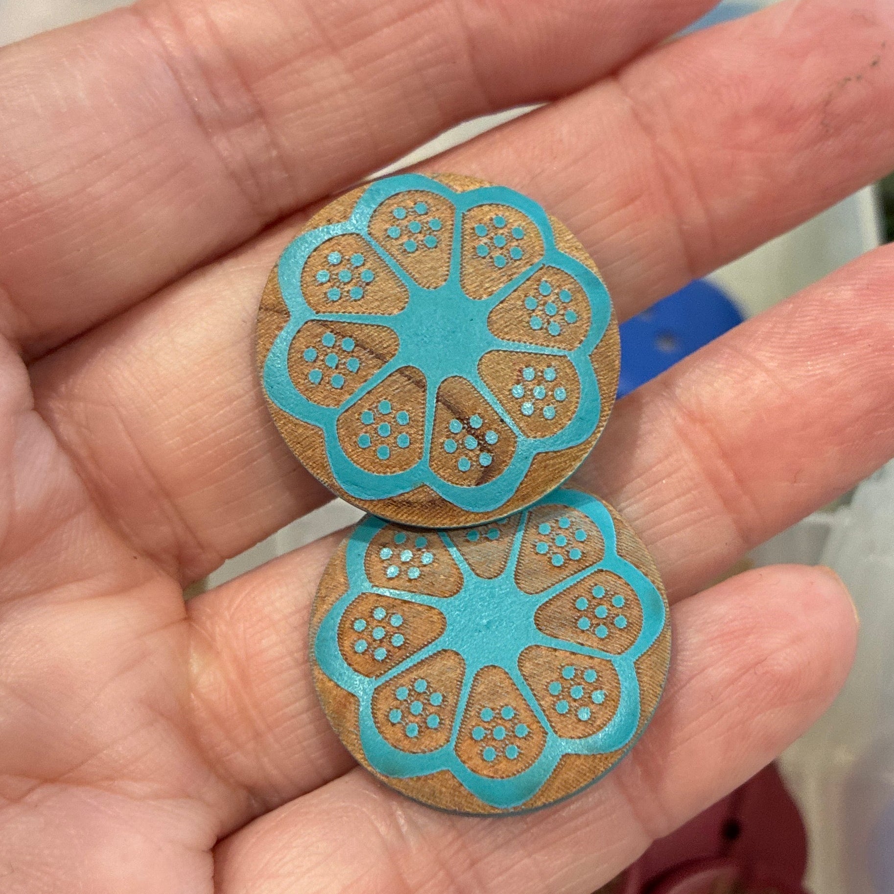 Hand holding two blue floral-patterned buttons with a background of assorted buttons.