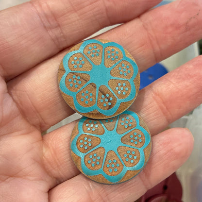 Hand holding two blue floral-patterned buttons with a background of assorted buttons.