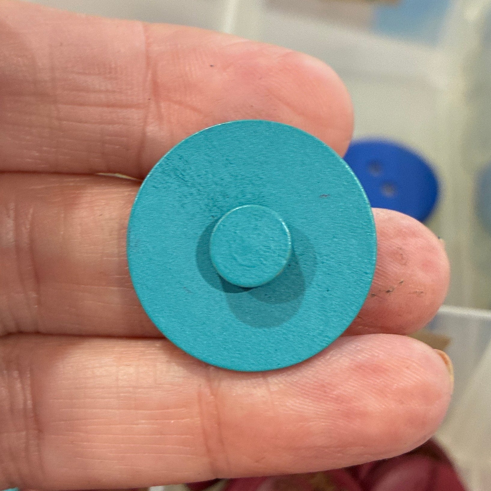 Hand holding a blue button with a container of colorful buttons in the background