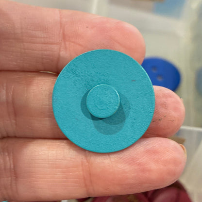 Hand holding a blue button with a container of colorful buttons in the background
