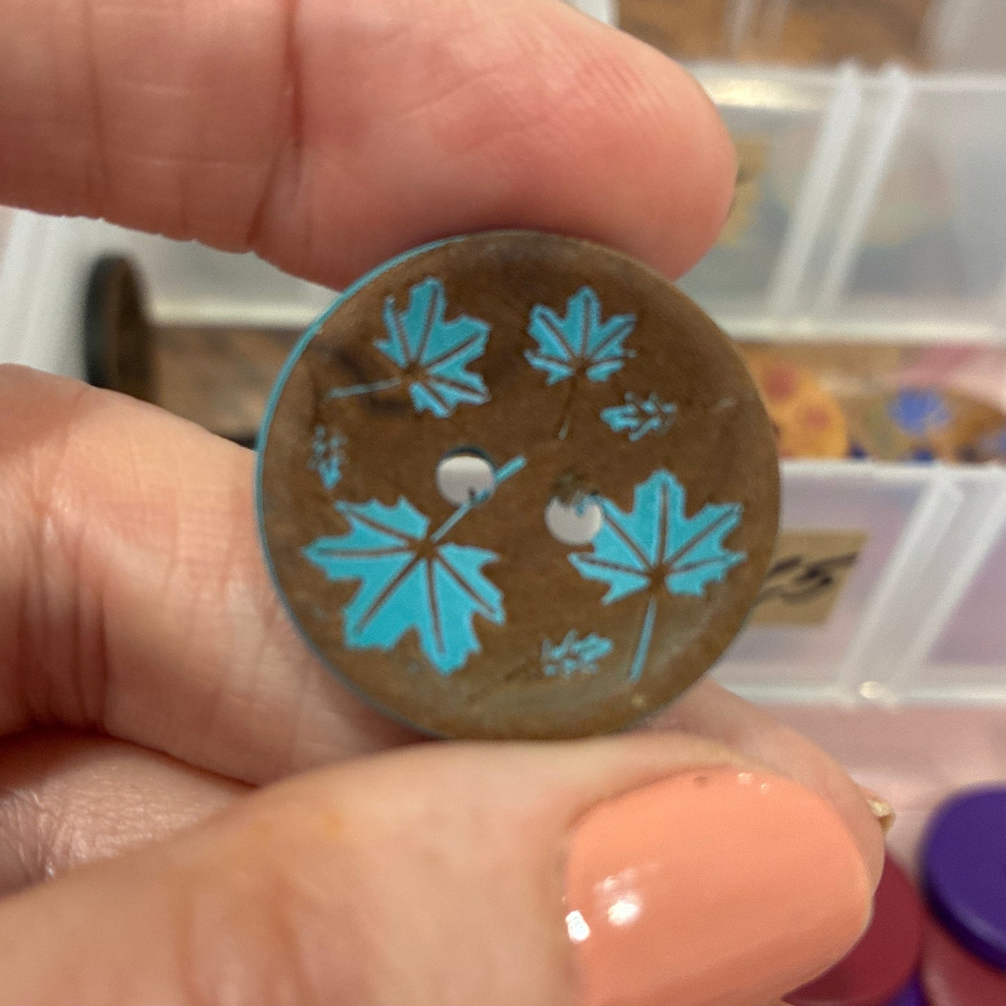 Hand holding a decorative button with blue floral patterns against a blurred background of buttons.