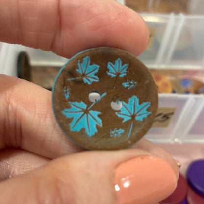 Hand holding a decorative button with blue floral patterns against a blurred background of buttons.