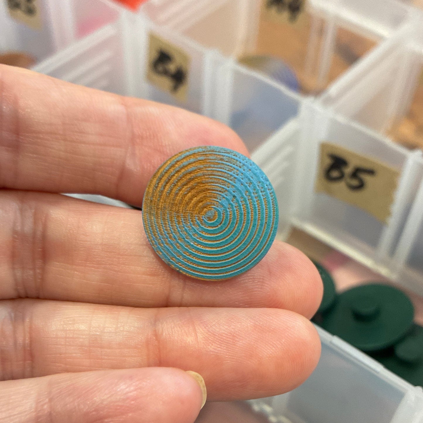 Hand holding a decorative button with a container of assorted buttons in the background
