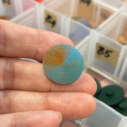 Hand holding a decorative button with a container of assorted buttons in the background