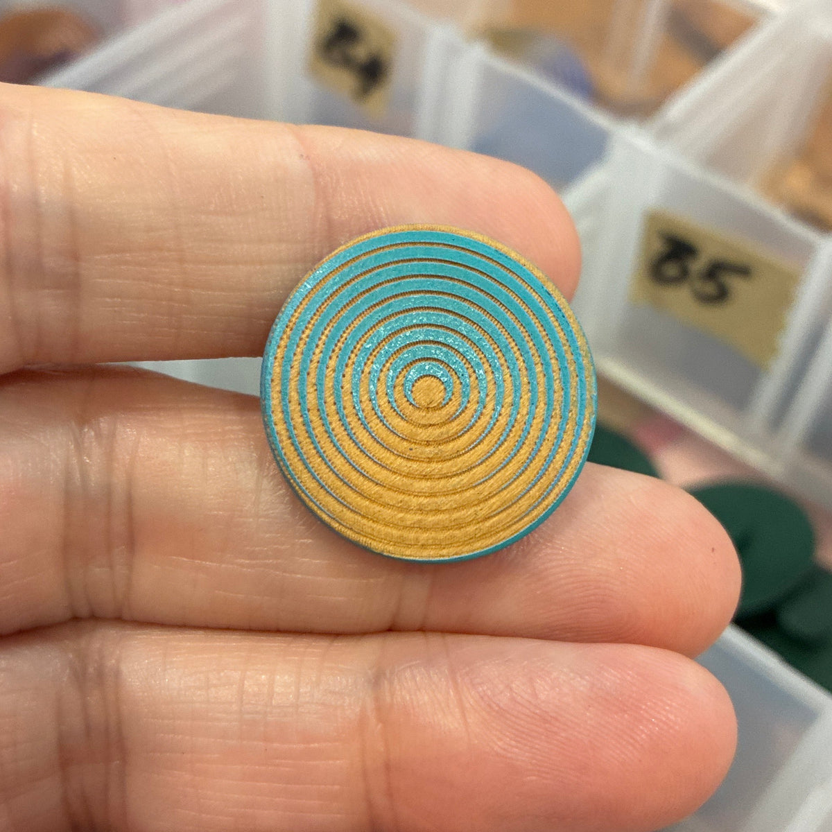 Gold spiral button held between fingers with a background of an open jewelry organizer.