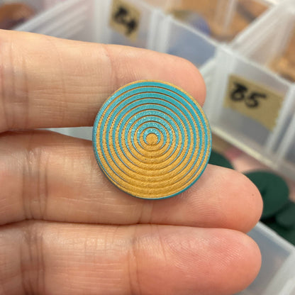 Gold spiral button held between fingers with a background of an open jewelry organizer.