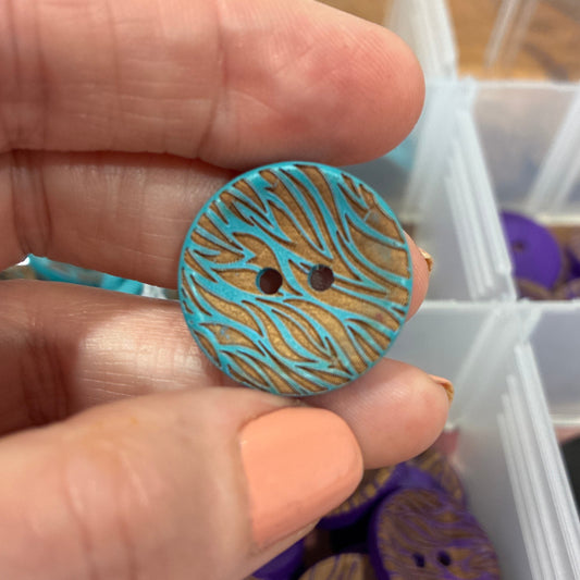 Hand holding a blue and gold button with a container of buttons in the background